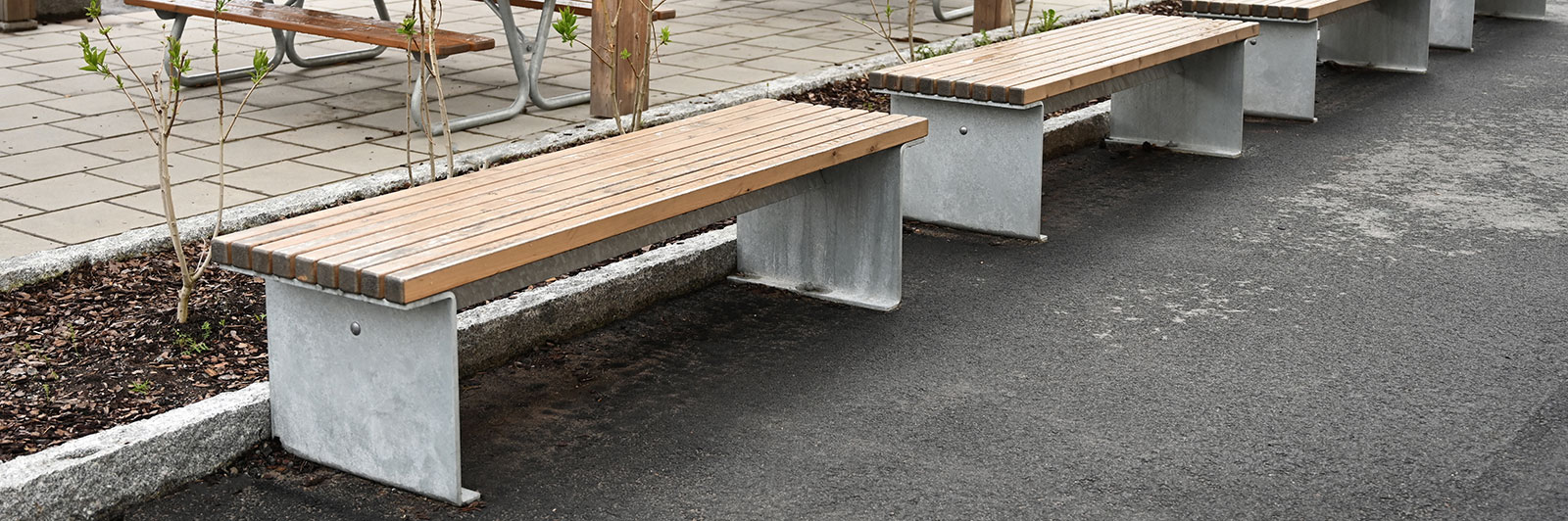 A row of standalone park benches with metal frames and wooden benches.